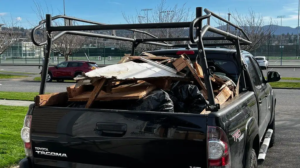 A black pickup with a ladder rack, its bed piled with wood scraps, old siding and black garbage bags