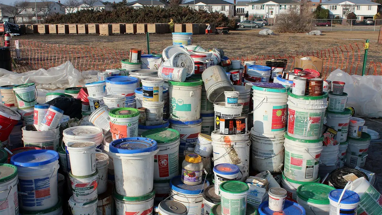 Rows of used paint pails and cans stacked on plastic sheeting at an outdoor hazardous waste collection area