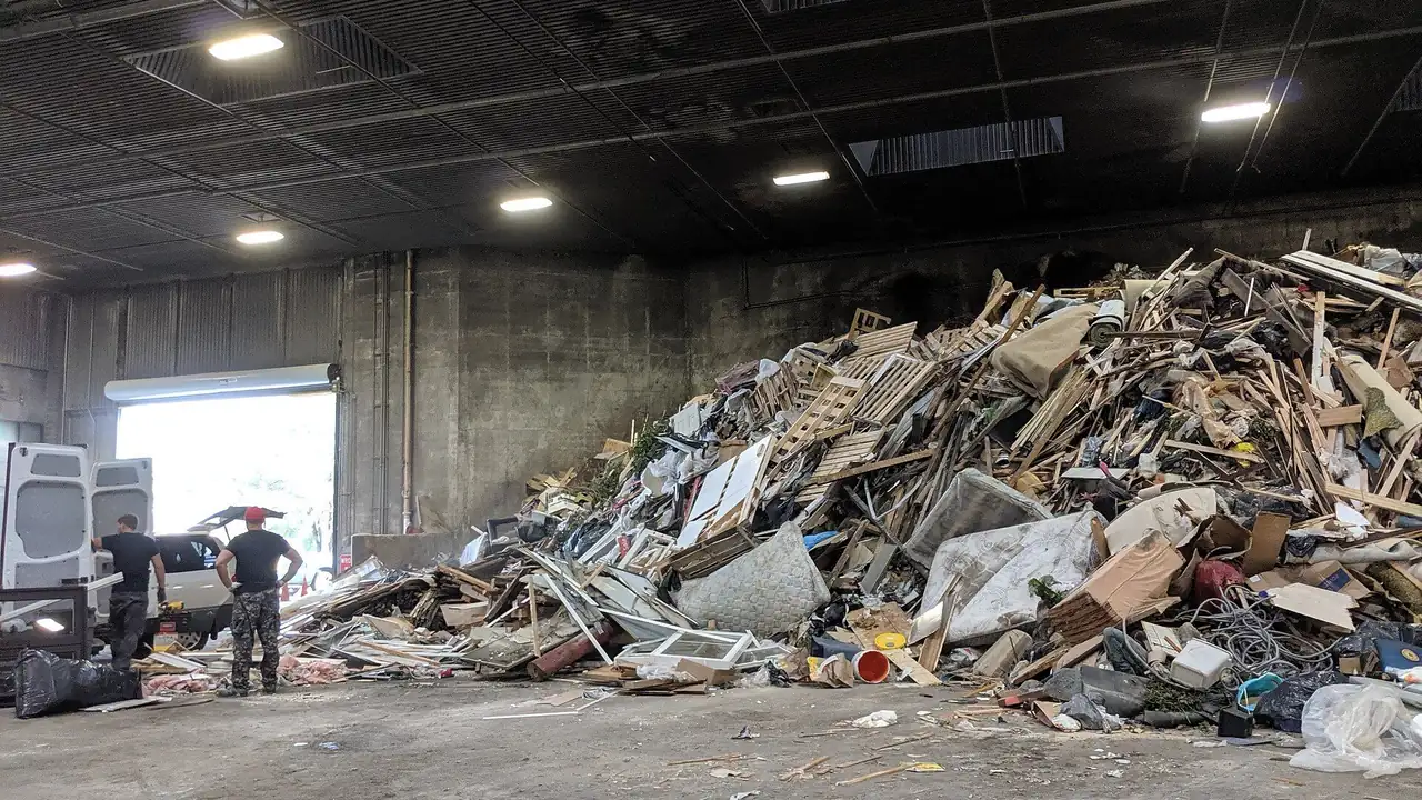 Two people unloading a white cargo van beside a pile of renovation waste on the tipping floor at Ingram Transfer Station