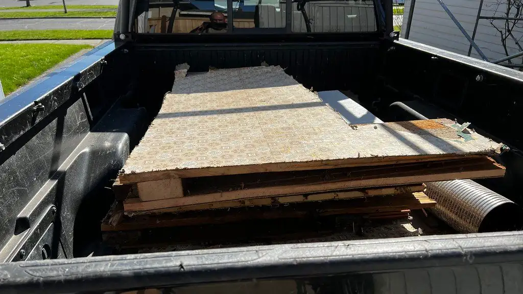 Sheets of old flooring and boards stacked flat in the bed of a pickup truck