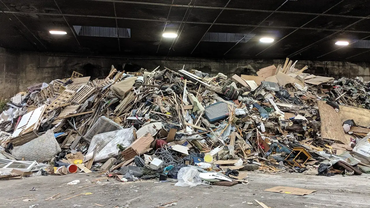 A large pile of broken lumber, pallets and bagged waste on the concrete tipping floor inside Ingram Transfer Station